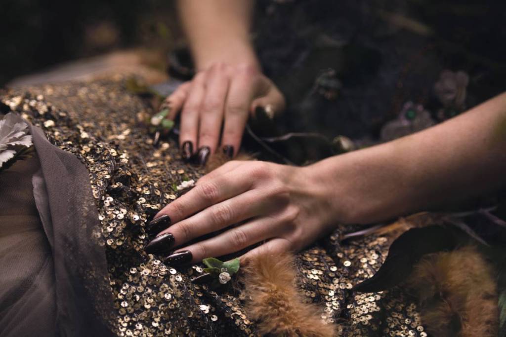 manicured hands touching a piece of clothing made with sequins and fur