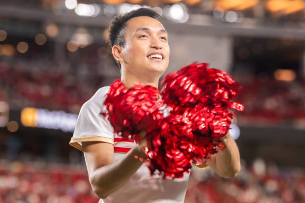 male cheerleader holding red pom poms