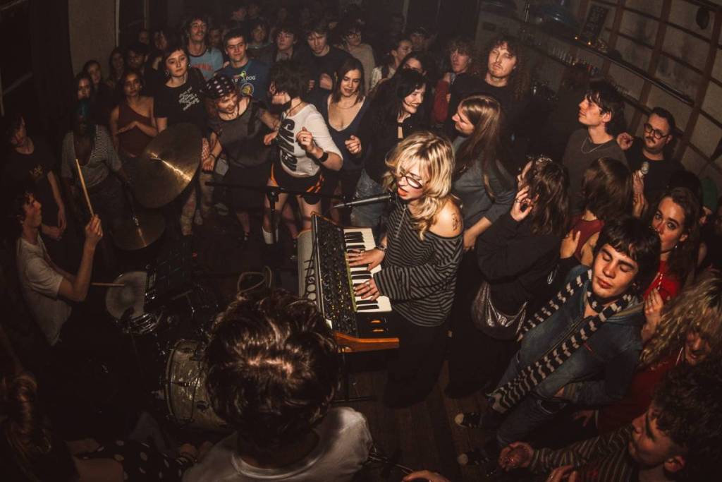 musicians playing key board and drums surrounded by close listeners