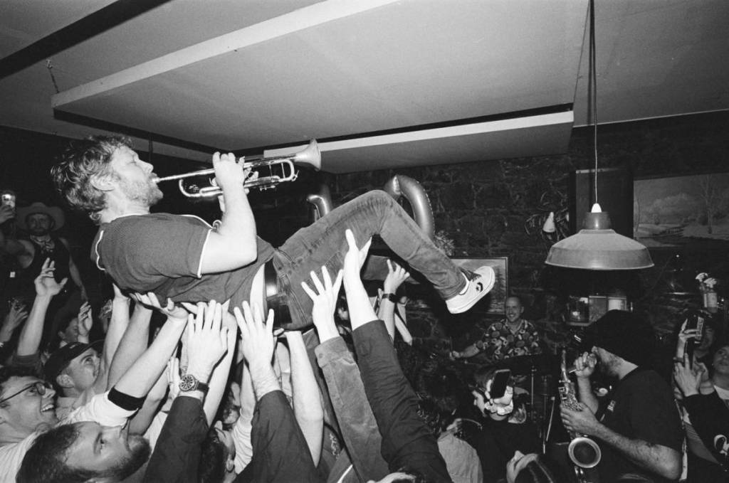 man playing trumpet while held up by crowd