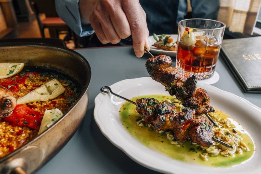 a hand reaching to pick up a meat skewer at Movida Aqui restaurant