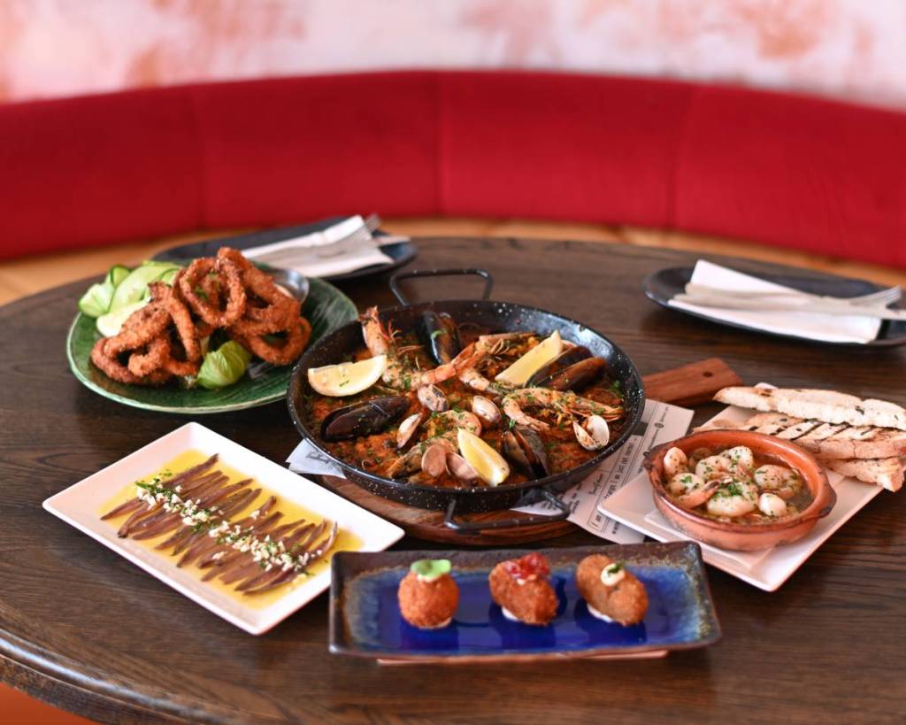 a table laden with paella and other tapas including croquettas and gambas at Manolo Bar