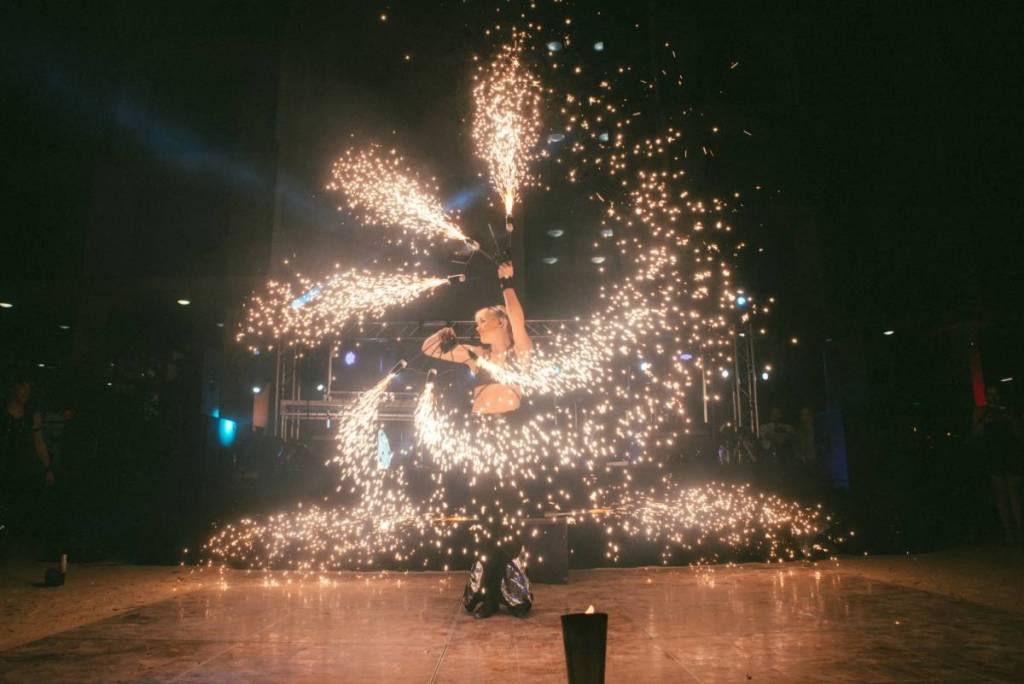 circus performer spinning multiple sticks creating fiery sparks in a spiral