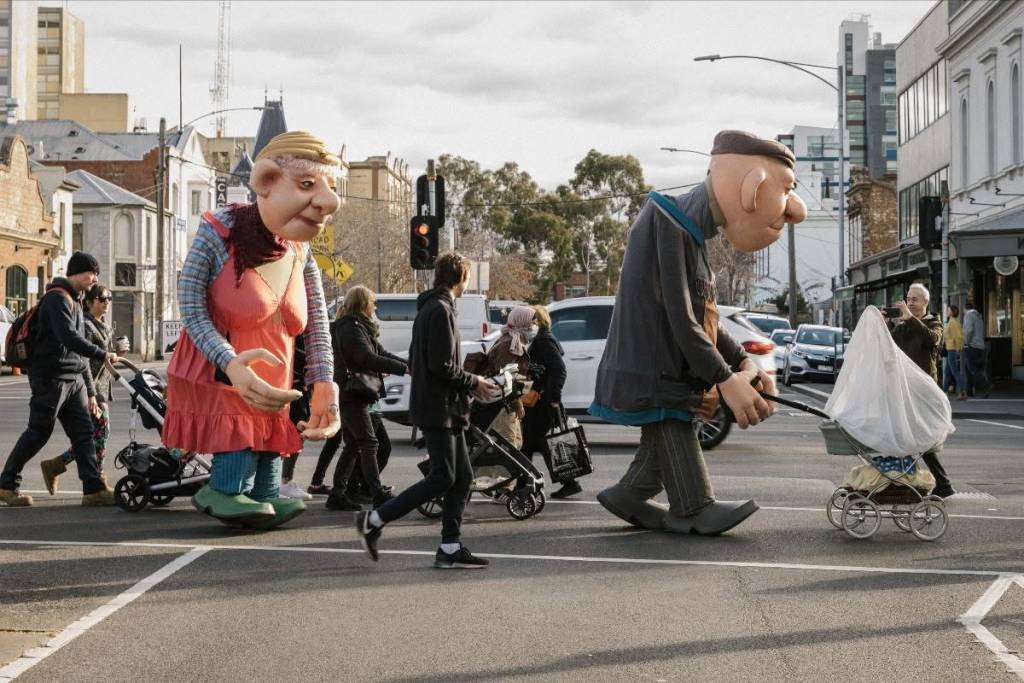 two roving large puppet performers crossing the street with normal people