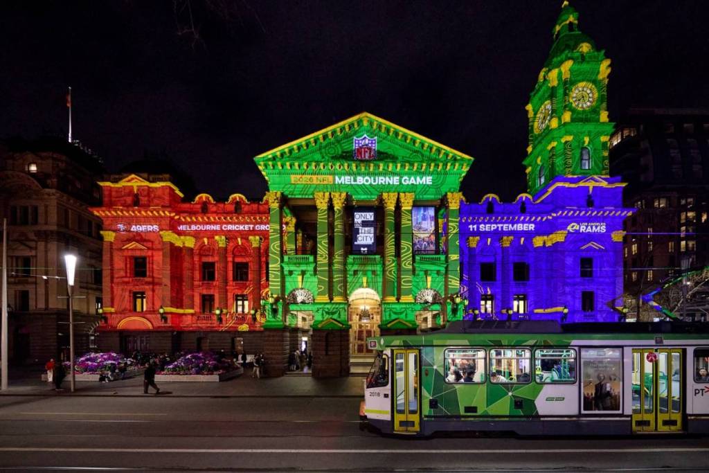tram going by Melbourne Town Hall, which is lit up in projections to promote the NFL game