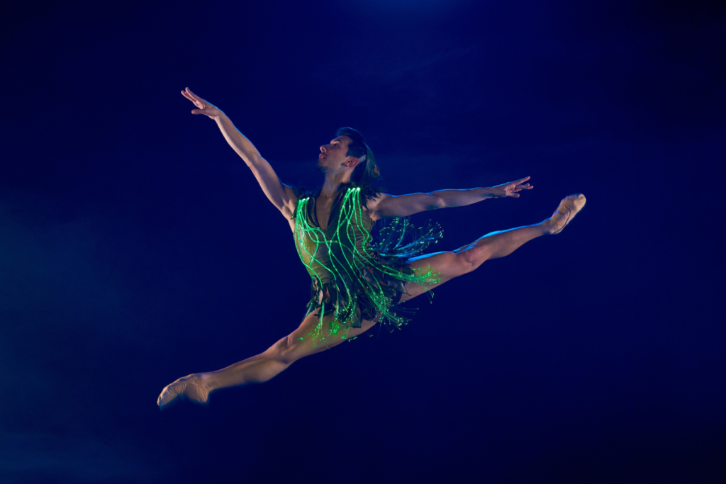 A ballet dancer in the role of Peter Pan, wearing a glow-in-the-dark costume and leaping on the stage