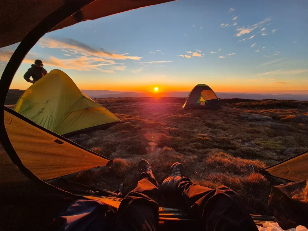 someone's feet outside a tent, looking at sunset surrounded by other tents, on Mount Bogong Loop trail
