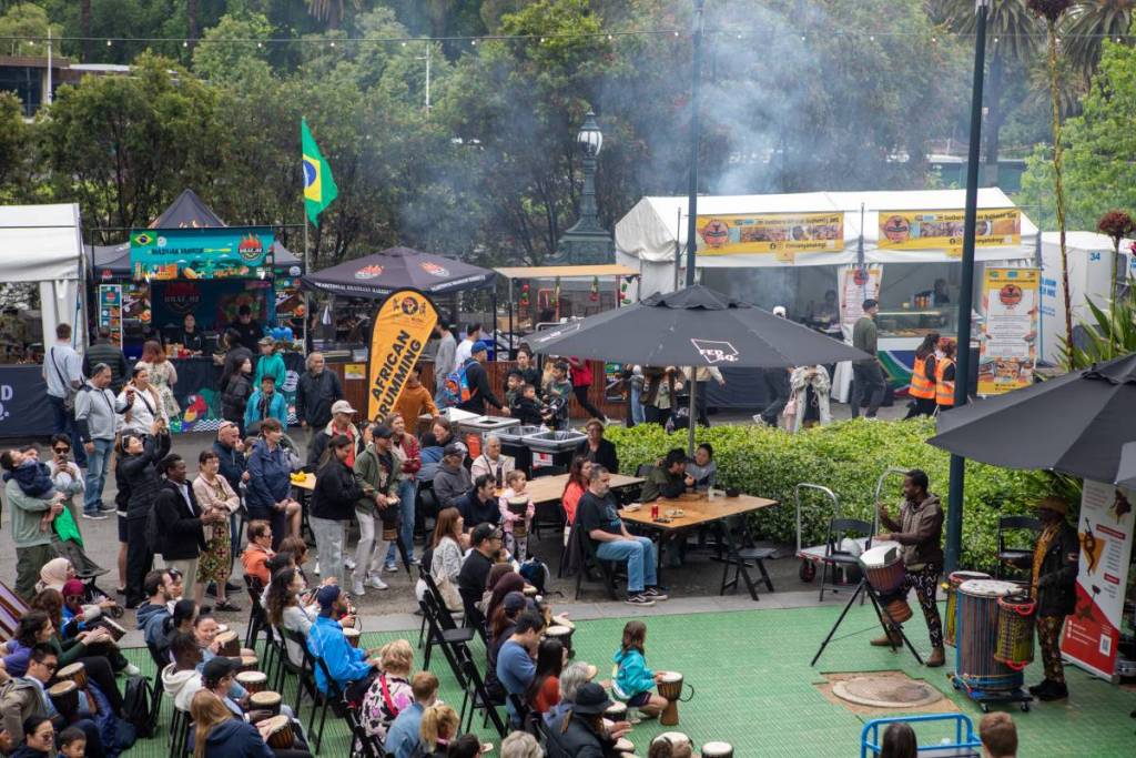 view of crowd taking part in drumming workshop, with food stalls in the background