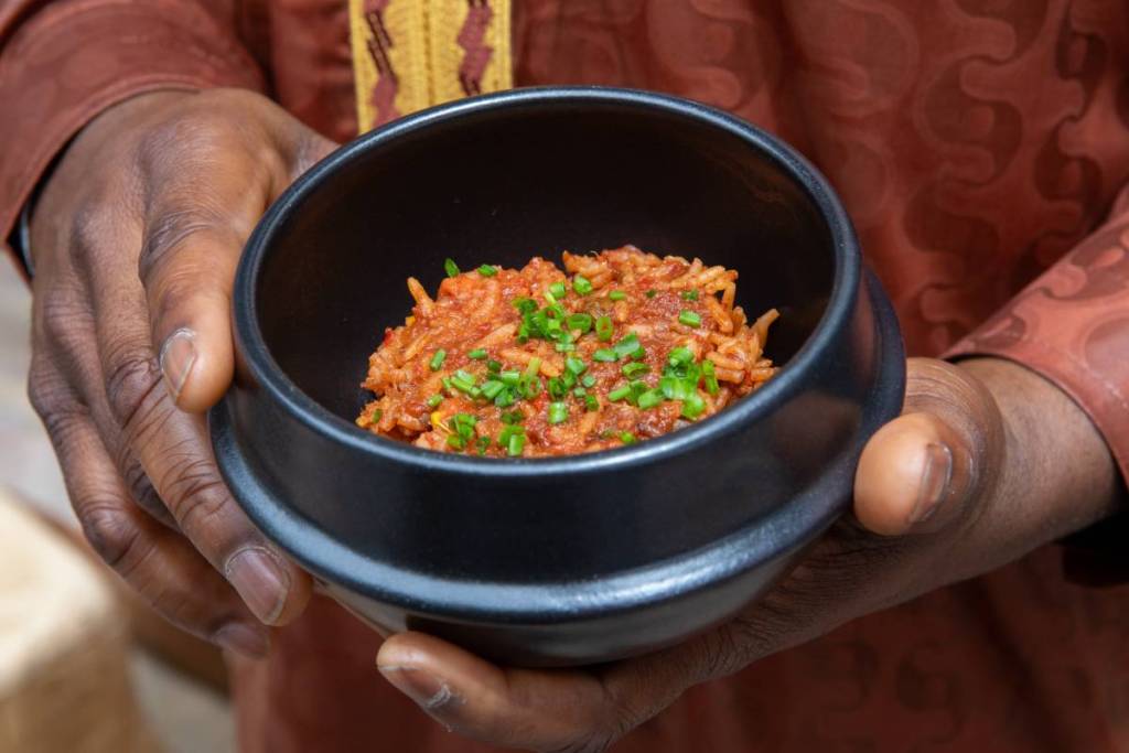 man's hands holding a bowl of jollof