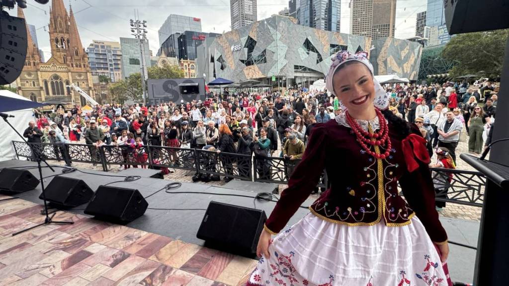 woman in traditional costume for Polish Festival on stage, with crowds at Fed Square behind her