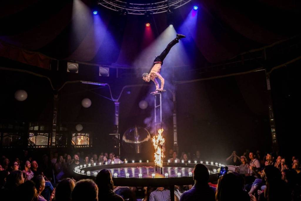 A man balances on his hands at the top of a ladder that's on fire at La Ronde.