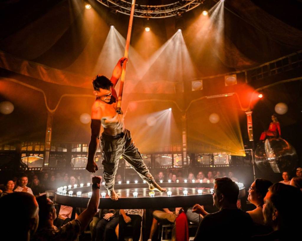 A performer hangs from a pole coming from the ceiling at La Ronde.