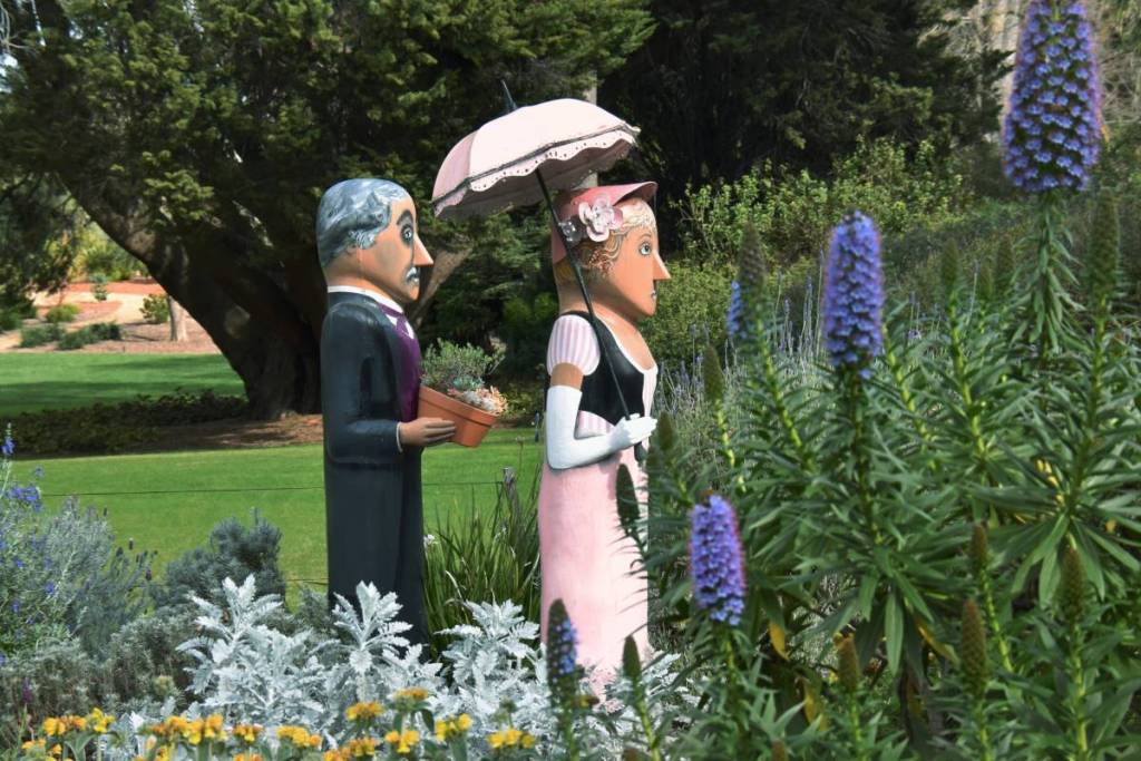 two bollard characters in old-timey costumes at Geelong Botanic Gardens, with flowers visible