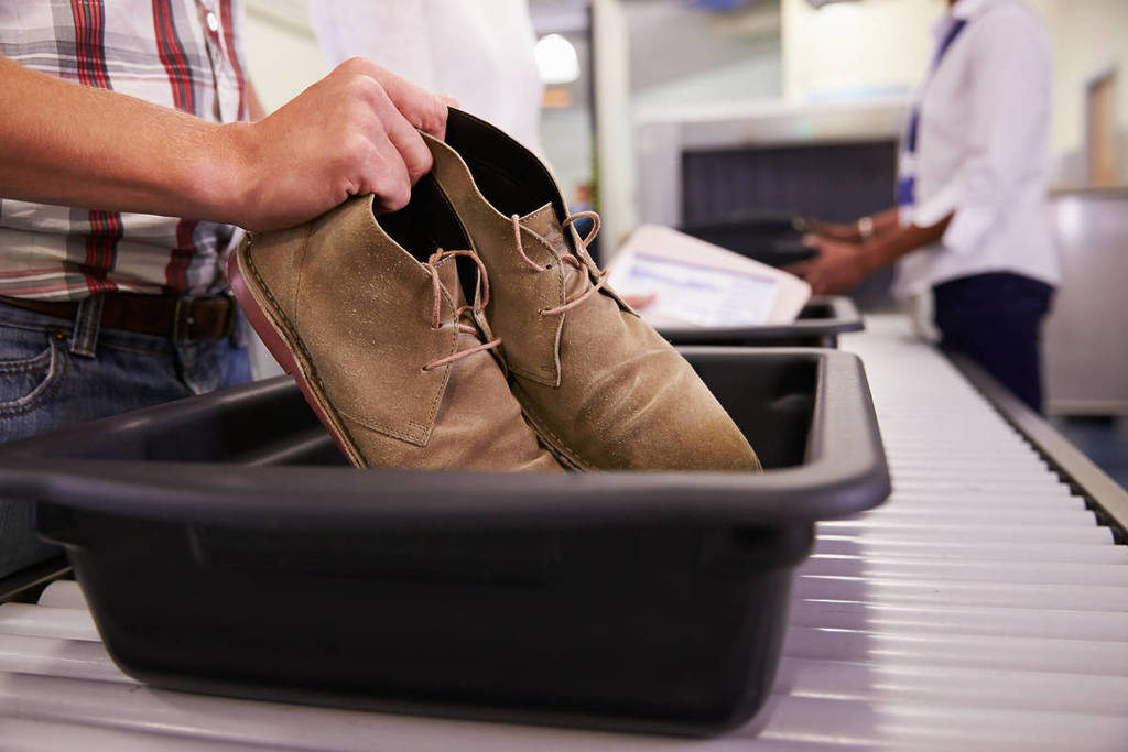 Homem coloca sapatos em bandeja para verificação de segurança no aeroporto
