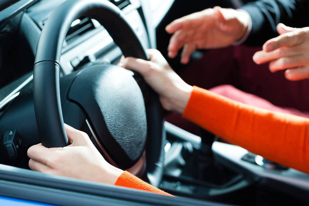 École de conduite - Une jeune femme conduit une voiture avec le volant, elle a peut-être un examen de conduite, elle s'exerce peut-être au stationnement...