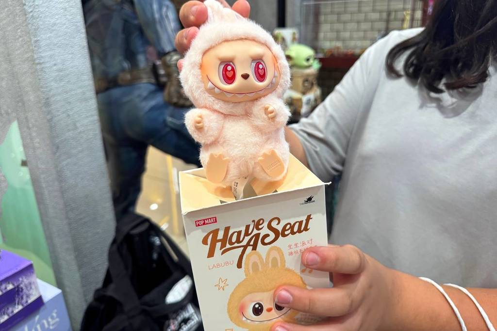 Close-up da figura de pelúcia Pop Mart Labubu Have A Seat com olhos vermelhos segurada por um cliente na loja.