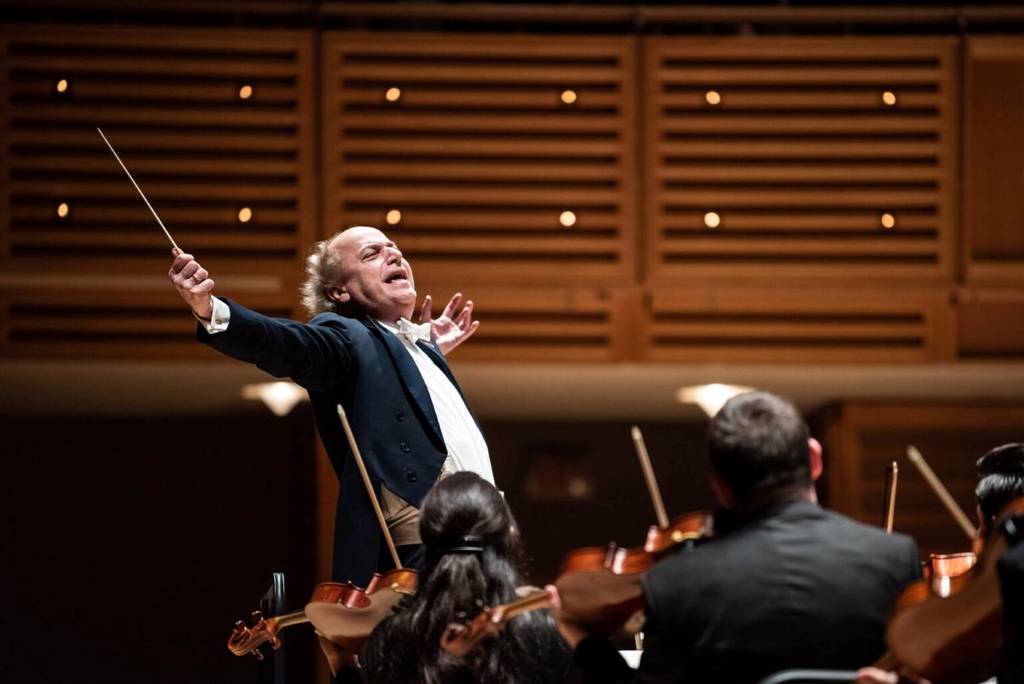 conductor of miami symphony orchestra stands in front of orchestra