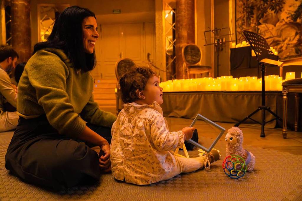 baby sits on floor beside her mother at candlelight baby concert