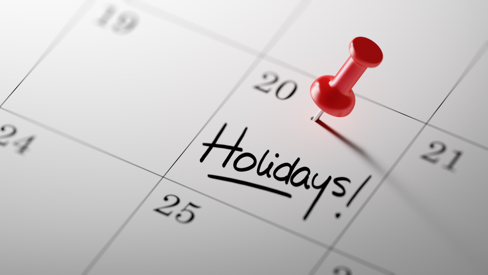 Concept image of a Calendar with a red push pin. Closeup shot of a thumbtack attached. The words Holidays written on a white notebook to remind you an important appointment.