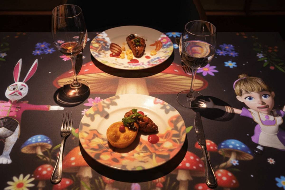 projection mapping on table shows characters from alice in wonderland and meal