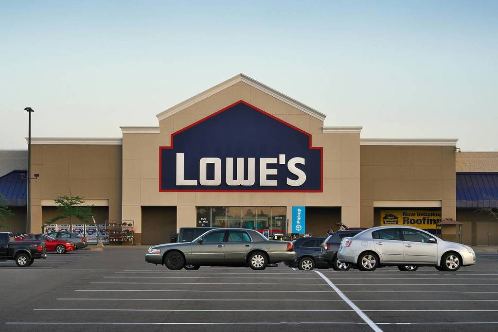 Vista frontal da entrada de uma loja da Lowe’s com carros estacionados no estacionamento durante o dia