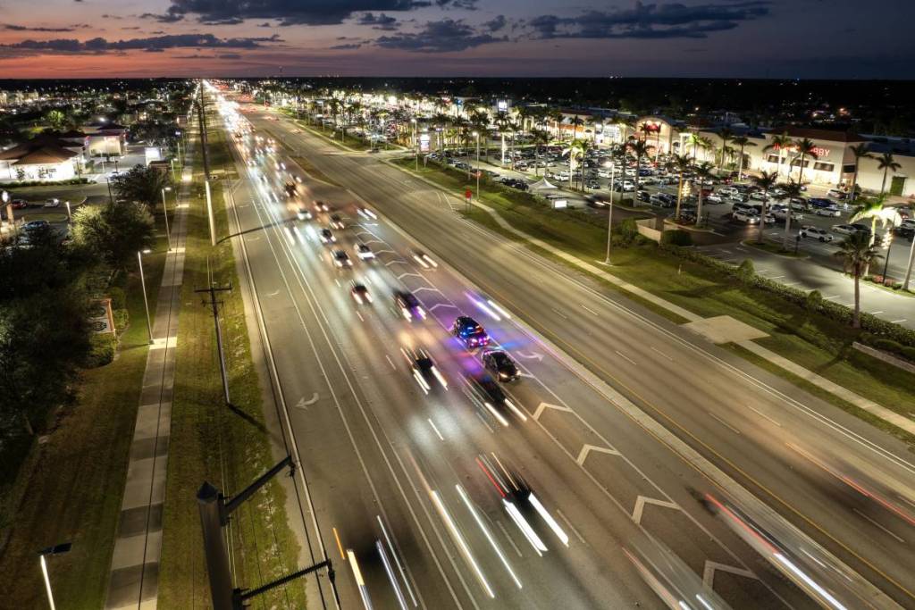 Un agente de policía detiene a un conductor que circulaba a exceso de velocidad por una calle estadounidense por la noche. Las luces de emergencia iluminan la carretera urbana con el tráfico a su alrededor. North Port, Florida, EE. UU.