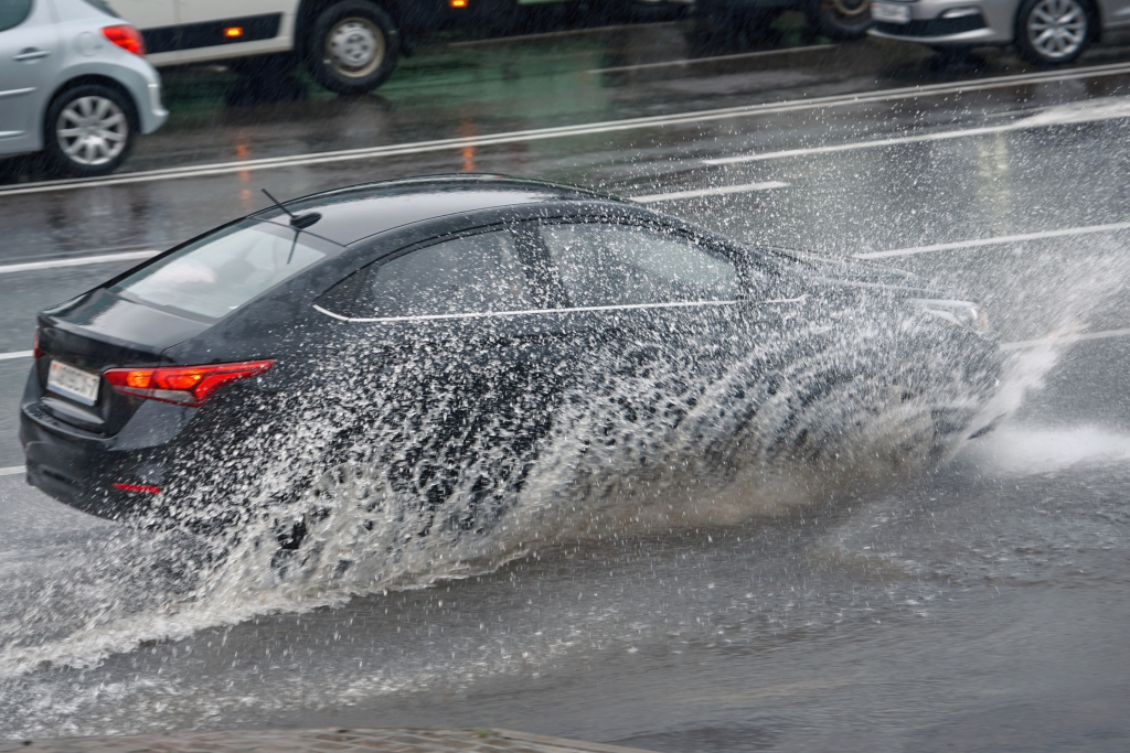 Un coche salpicando agua al pasar por un charco bajo una lluvia intensa