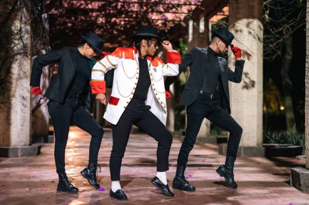 Tres hombres con trajes de baile a la última y sombreros posando de forma dramática al aire libre por la noche.