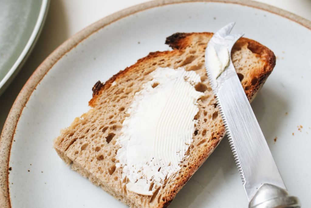 A close-up of buttered bread with a knife on a ceramic plate, perfect for a breakfast scene.
