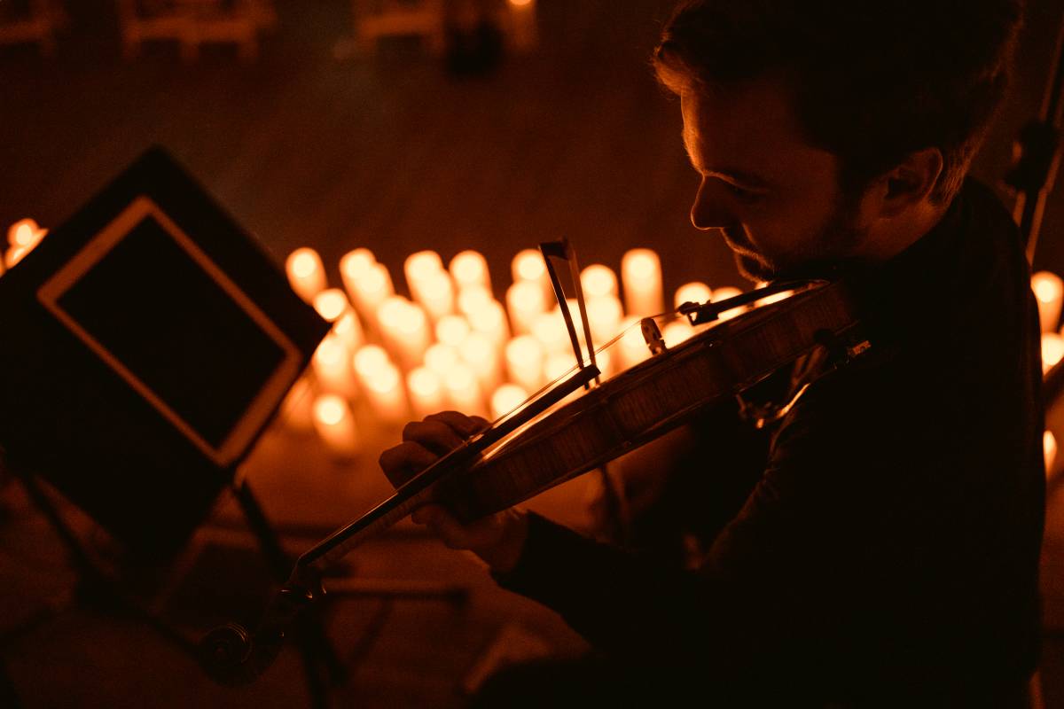 A close-up of a musician playing a violin with candles in the background.