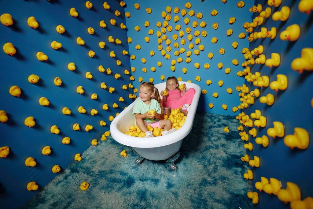 Two girls in a bath tub selfie room surrounded by rubber ducks at Bubble Planet