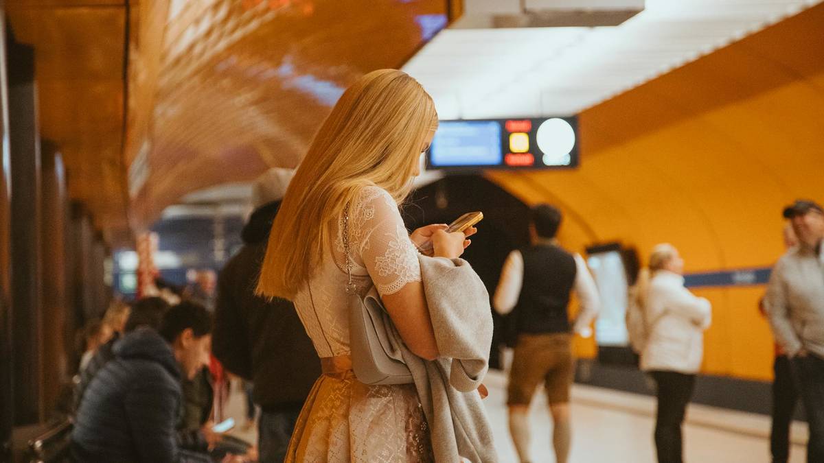 Frau im Dirndl steht am U-Bahnhof mit dem Smartphone in der Hand