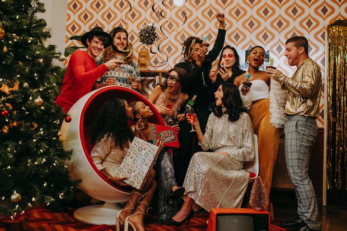eine Gruppe von Freunden feiert Weihnachten zusammen und stößt in festlich dekorierter Umgebung gemeinsam neben einem Weihnachtsbaum an
