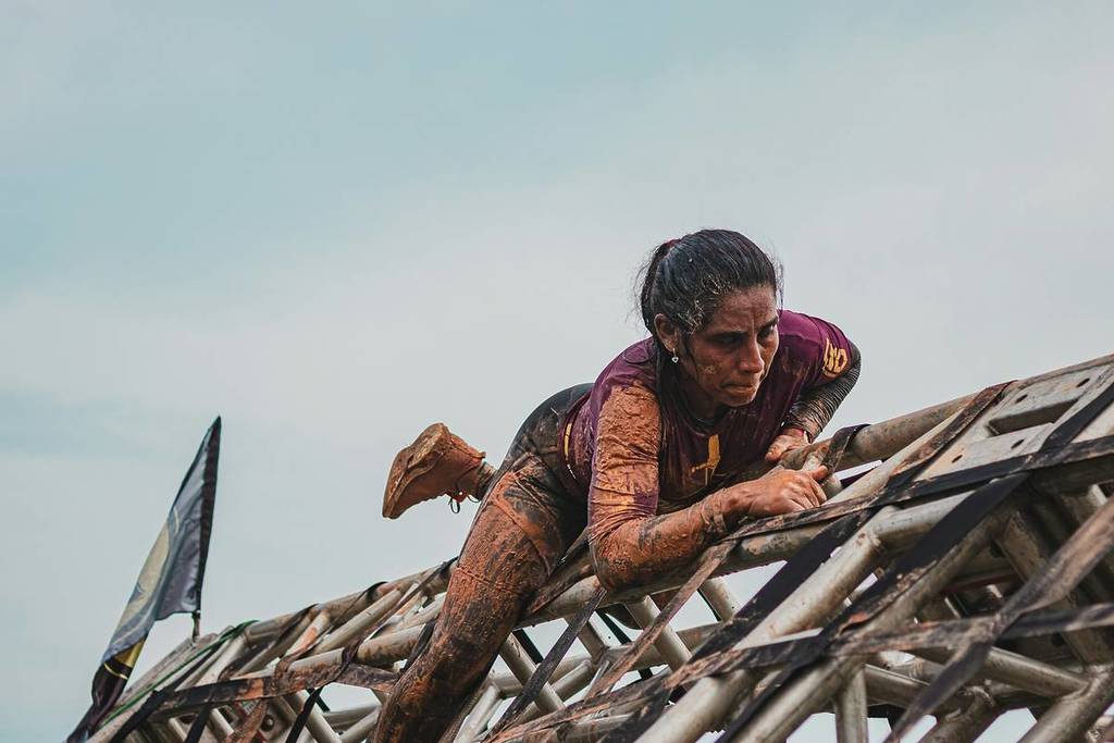 mud-covered woman climbing over an obstacle