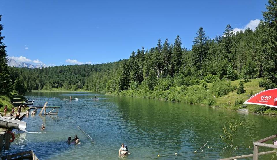 Nur 85 Minuten von München badet ihr in einem idyllischen Bergsee mit einer 40 Meter langen Wasserrutsche, Sprungturm, Kinderbecken und Tretbootverleih