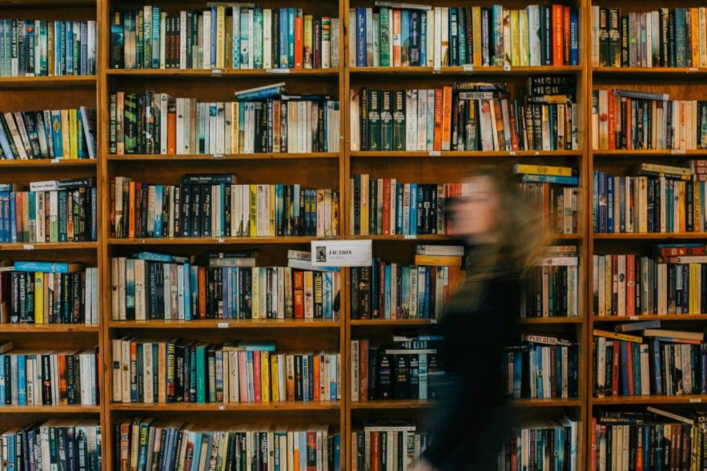 frau läuft an bücherregal in buchhandlung vorbei