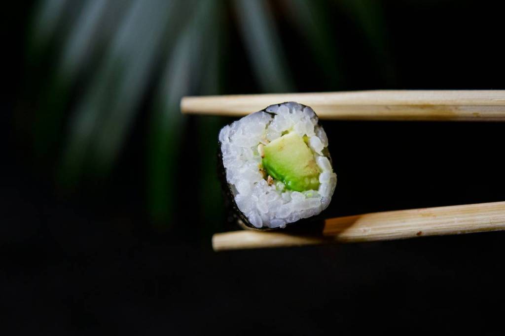 person hält avocado maki mit stäbchen
