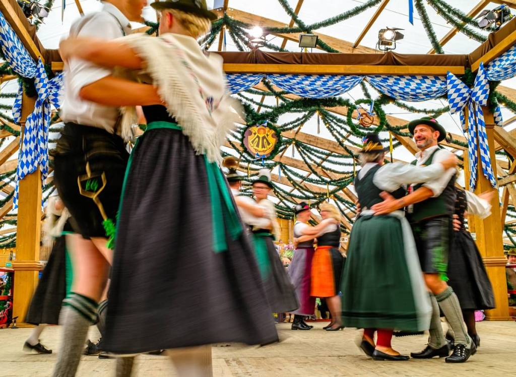 leute tanzen in hirstorischer tracht in einem oide wiesn zelt