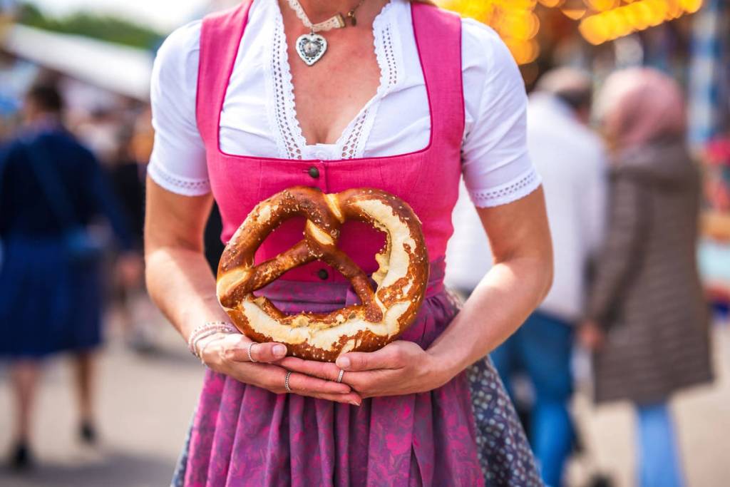 Frau im pinken Dirndl hält eine Brezel
