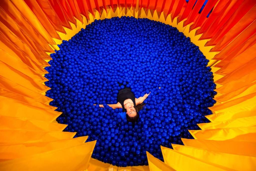 Frau liegt in einem blauen Bällebad bei "Dream Rooms", umgeben von einem orangenen Vorhang