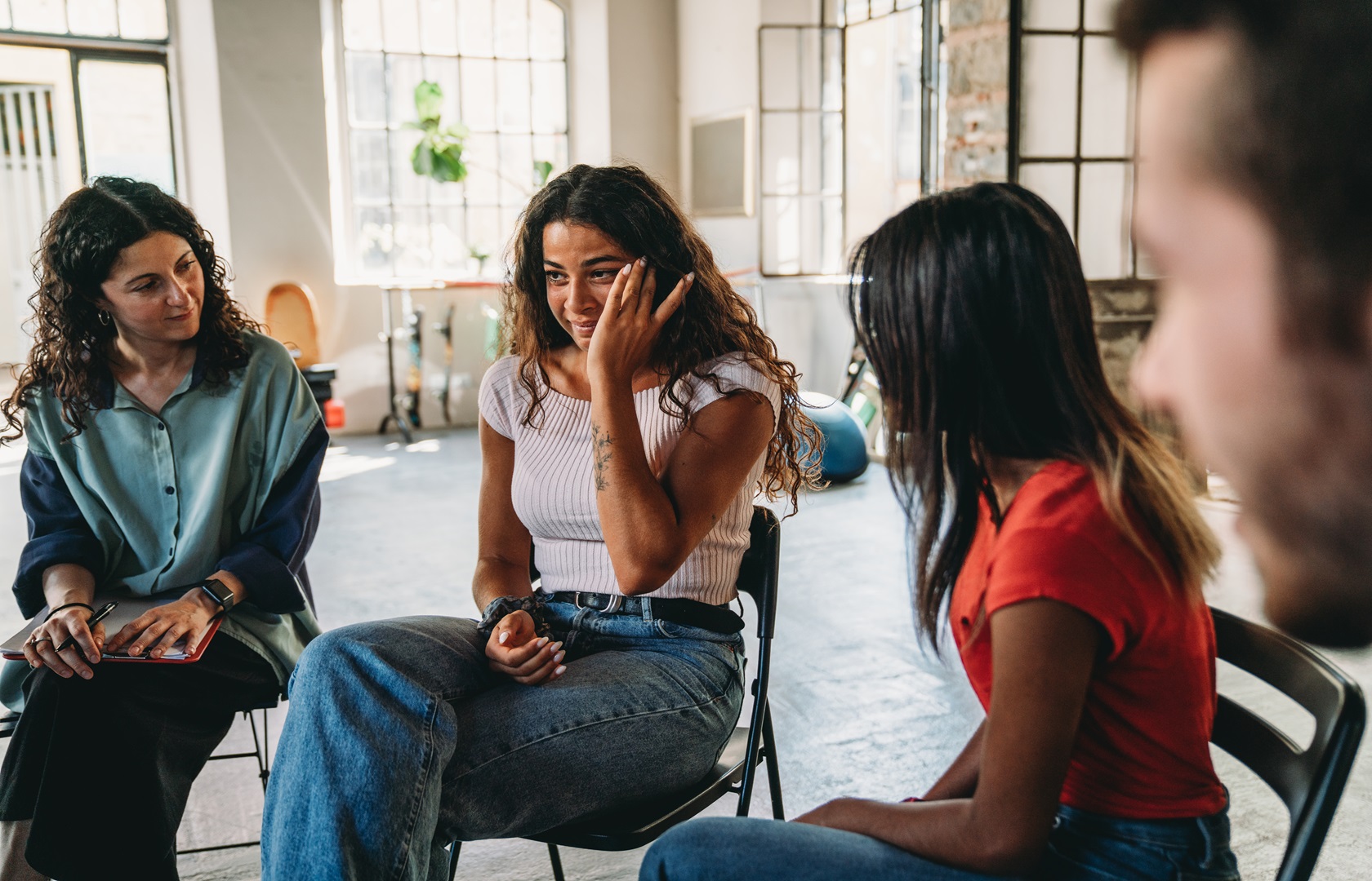 A woman is crying during a group therapy session. Mental health concept in a loft with big windows. Healthcare and medicine concept. Group of people sitting in a circle are participating in a support meeting, talking with each other like in the crying club