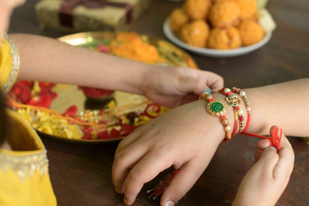 a siter tying her brother rakhi on raksha bandhan with sweets and aarti thali in background