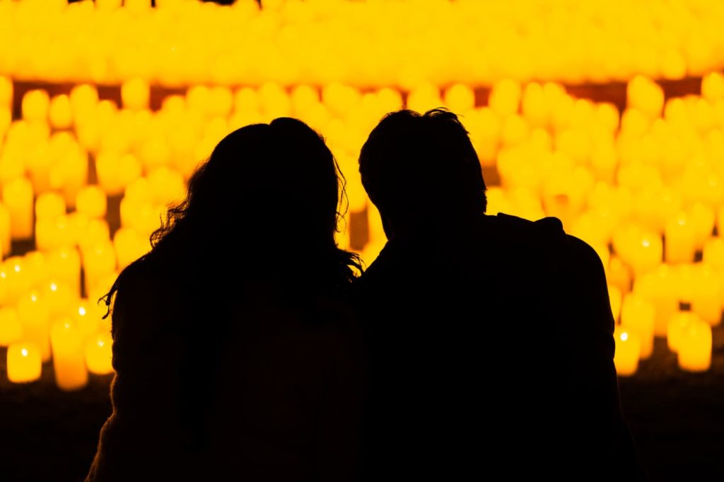 couple with their backs to the camera look at sea of candles
