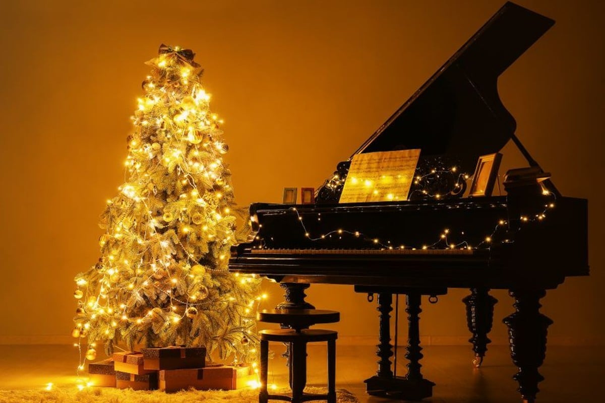 Pianoforte illuminato vicino ad un albero di Natale in un concerto candlelight