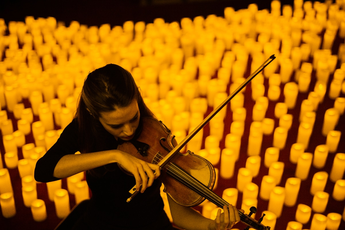 A violinist plays, surrounded by candles.