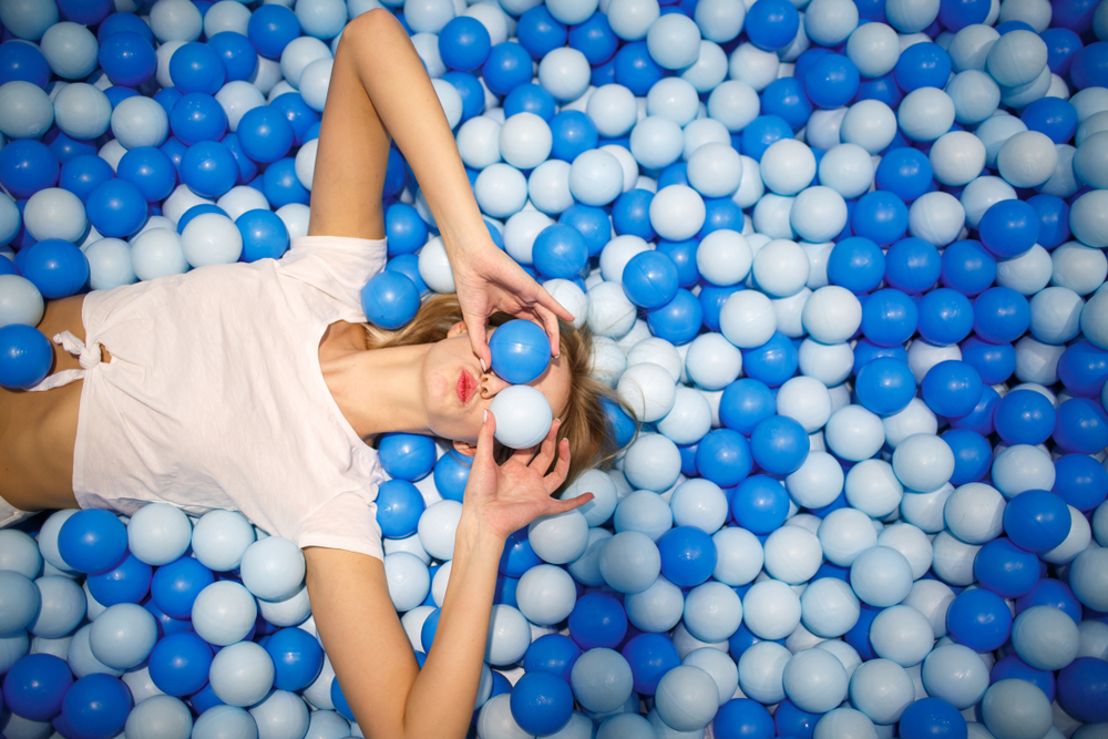 Woman playing in a ball pit, using the balls to cover her eyes.