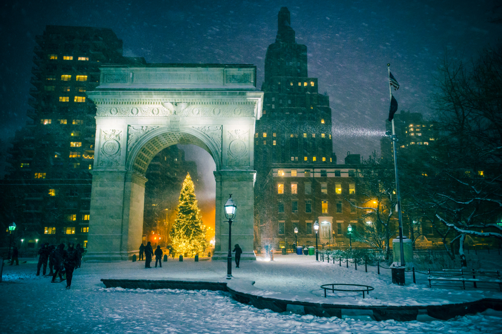 Winter holiday night view of the Washington Square Park with a Christmas Tree and snow on the ground.