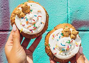 Two hands holding cookies with vanilla frosting, sprikles, and teddy grahams