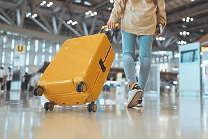 Female traveler passenger walking with a yellow suitcase at the modern Airport Terminal, Back view of woman on her way to flight boarding gate, Ready for travel or vacation journey