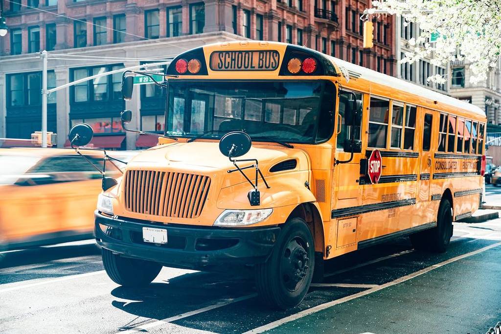 Ônibus escolar amarelo brilhante no cruzamento de uma rua movimentada de Manhattan, no centro da cidade de Nova York, perto de um carro de táxi em movimento